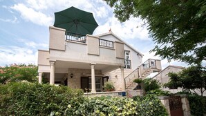 Een twee verdiepingen tellend huis met een overdekte veranda, een trap en een groene parasol.