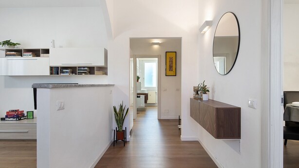 Cozinha moderna com eletrodomésticos embutidos, piso de madeira e um corredor que leva a uma sala de jantar.