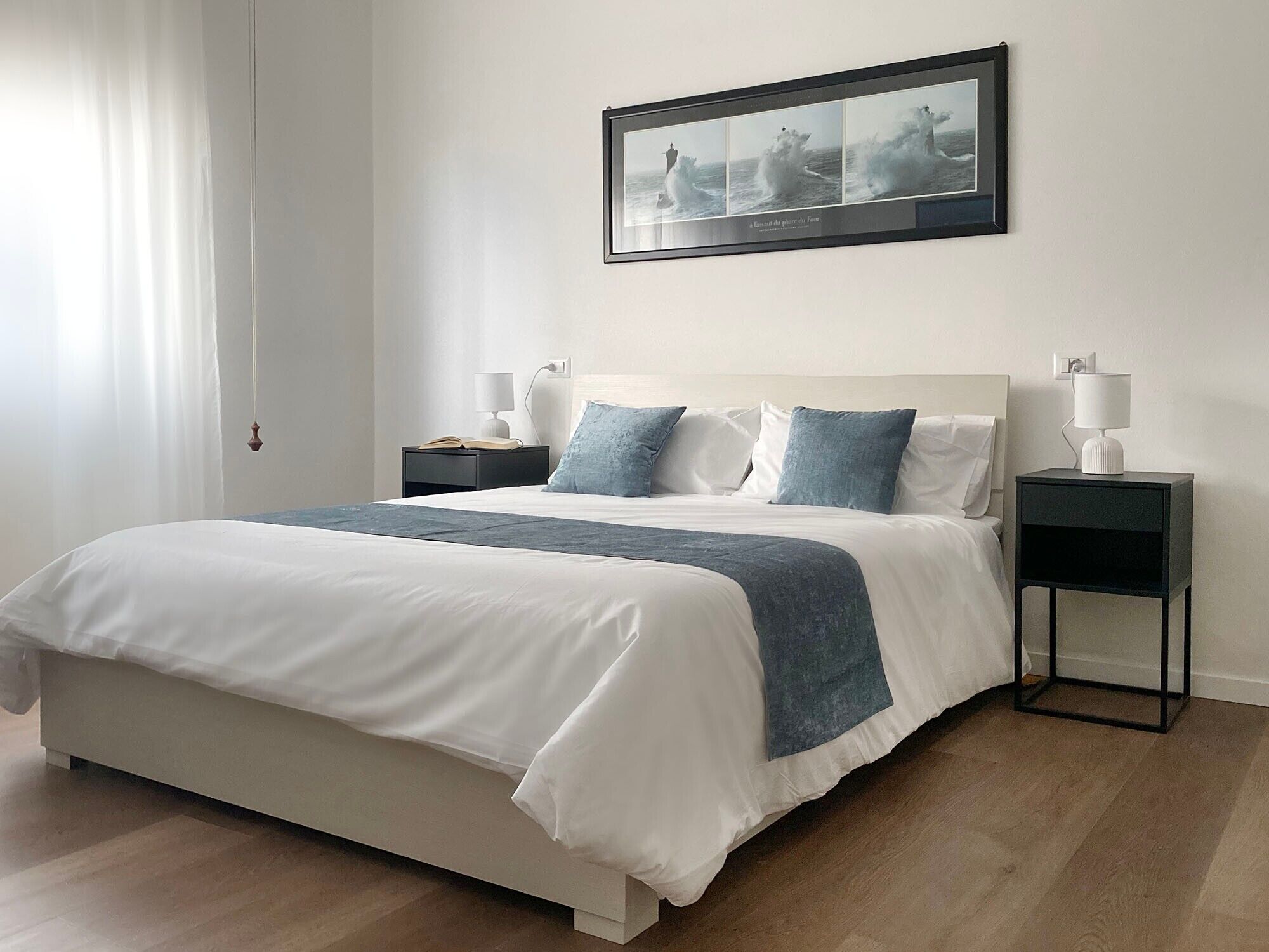 A modern bedroom with a large bed, two bedside tables, a nightstand, and a framed picture on the wall.