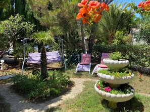 A garden with a swing set, lounge chairs, and a tiered planter with flowers. - Apartments Dali (Nin)