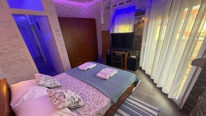 Ein Schlafzimmer mit Bett, Fernseher, Kleiderschrank und einem Fenster mit Vorhängen.