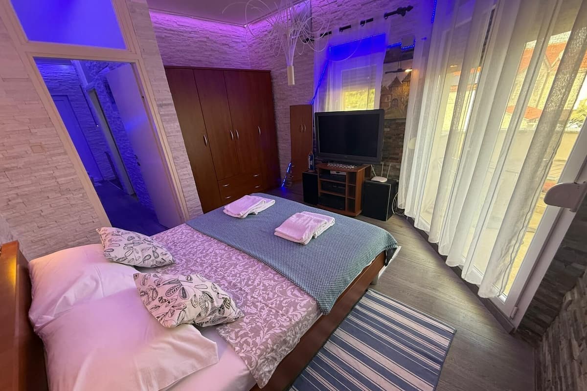 A bedroom with a bed, a TV, a wardrobe, and a window with curtains.