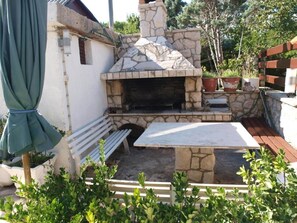 An outdoor patio with a stone-built oven, a wooden table, and benches. - Apartments Dali (Nin)