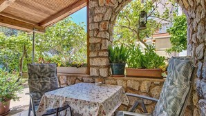 An outdoor patio with a stone arch, a table with a floral tablecloth, and two patterned chairs. - Apartments Pero (Mali Losinj)