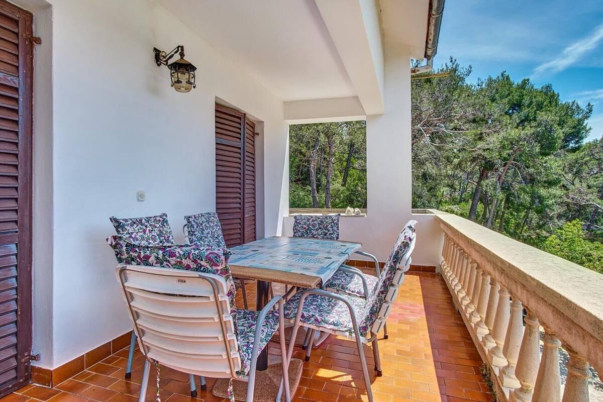 A covered outdoor seating area with a table and chairs, a railing, and a view of trees.