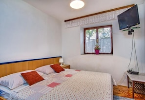 Ein Schlafzimmer mit einem Bett, einem Nachttisch, einem Fernseher und einem Fenster mit einer Pflanze.