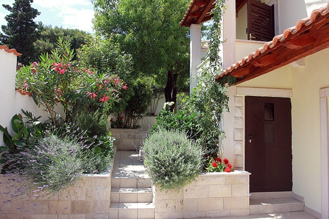 Une cour intérieure avec un escalier en pierre menant à une porte, le tout entouré de différentes plantes et arbres.