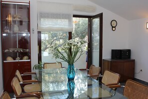 A dining area with a glass table, wicker chairs, a vase with flowers, a cabinet with decorative items, and a clock on the wall. - House Silvia (Supetar)
