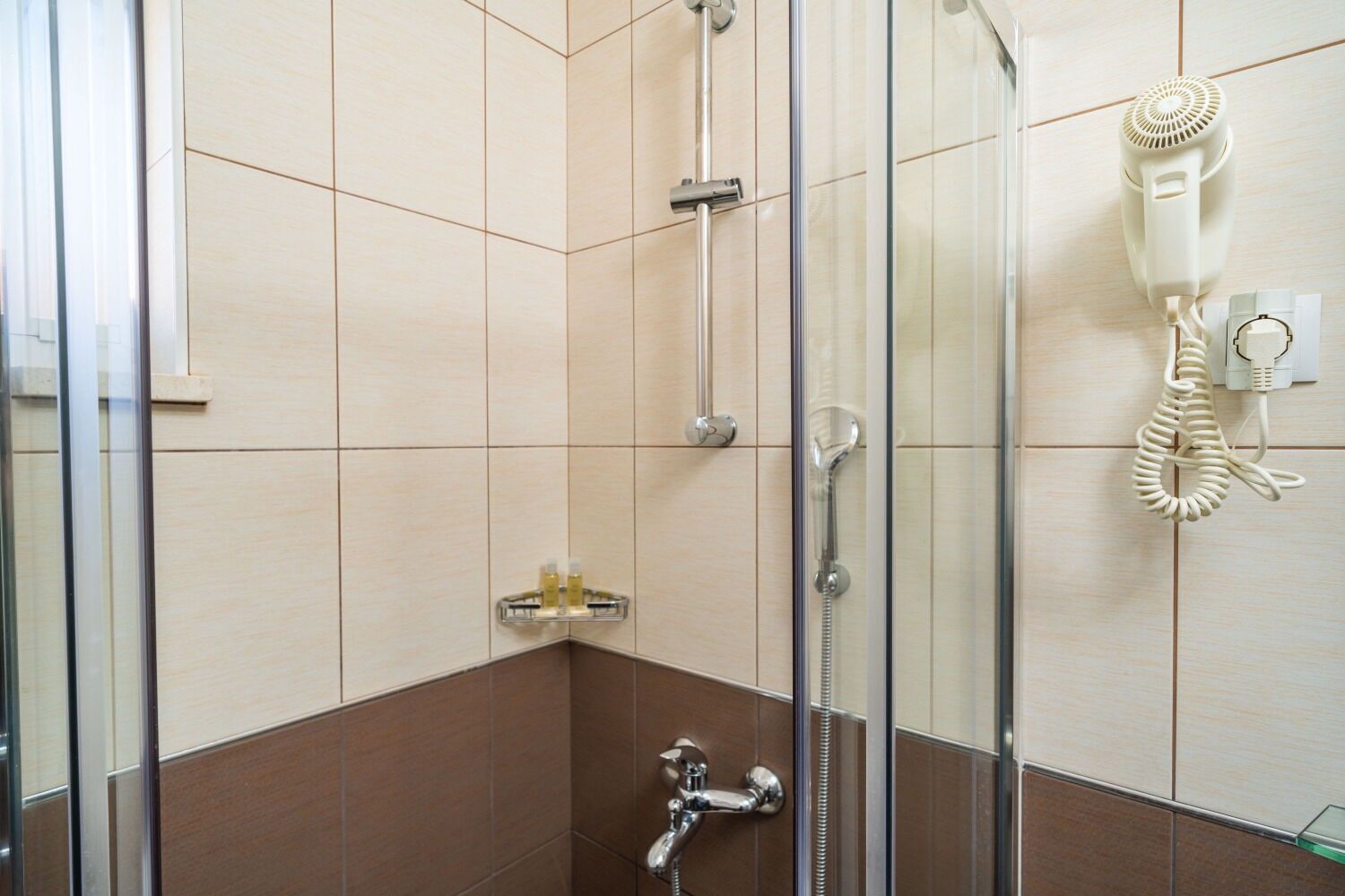 A modern bathroom with a glass shower enclosure, a handheld showerhead, a hairdryer mounted on the wall, and a towel rack.