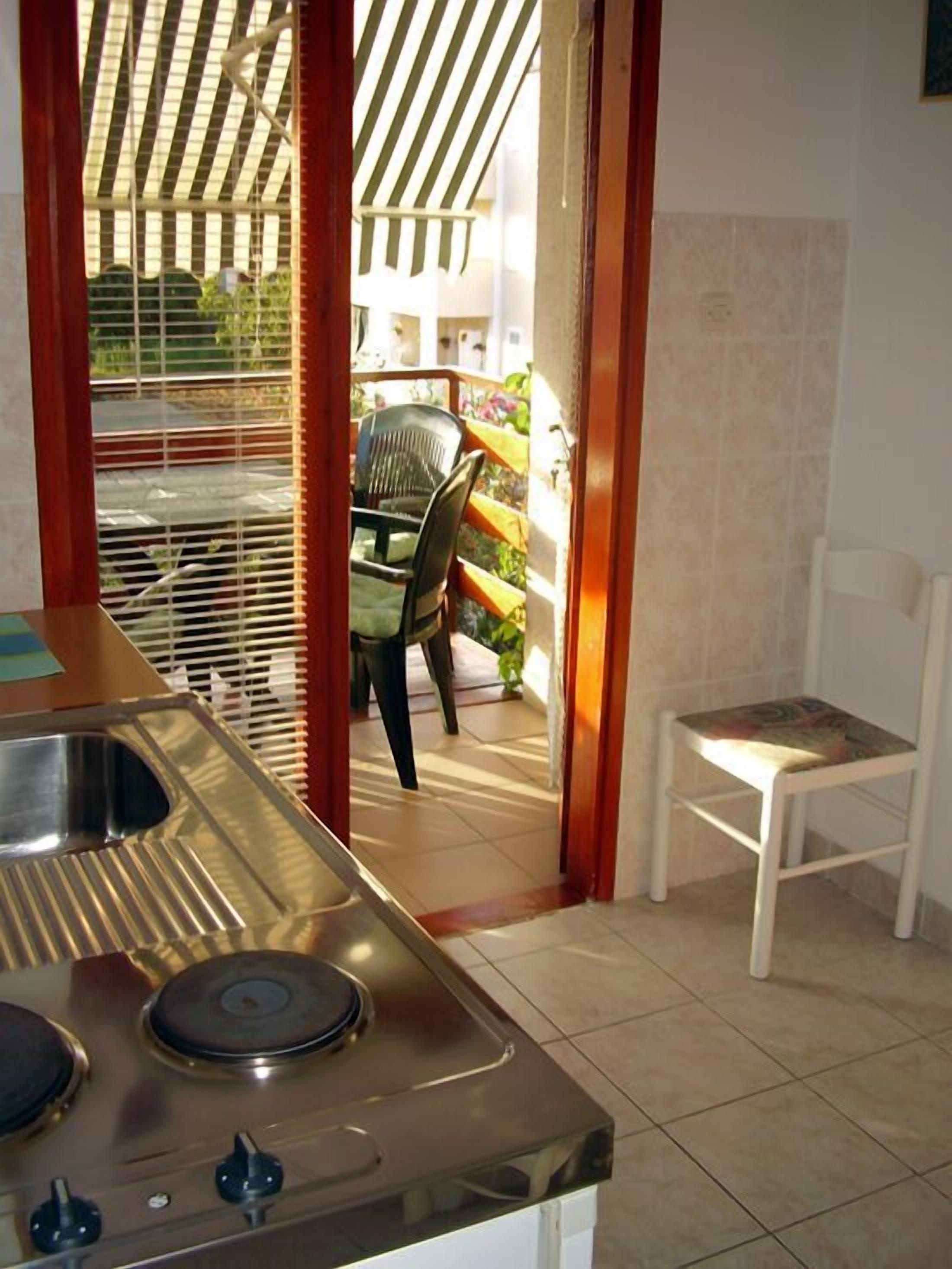 A kitchen with a sink and stove, a chair, and a view of a balcony with a chair and plants.
