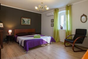 A bedroom with a bed, a chair, a lamp, a painting, and a window with curtains. - Apartment Alta (Makarska)