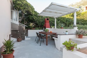 An outdoor patio with a table and chairs, a red barbecue grill, and potted plants. - Apartment Alta (Makarska)