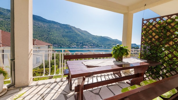 Un balcon avec une table et un banc en bois, un pot de fleurs et une vue sur un lac et des montagnes.