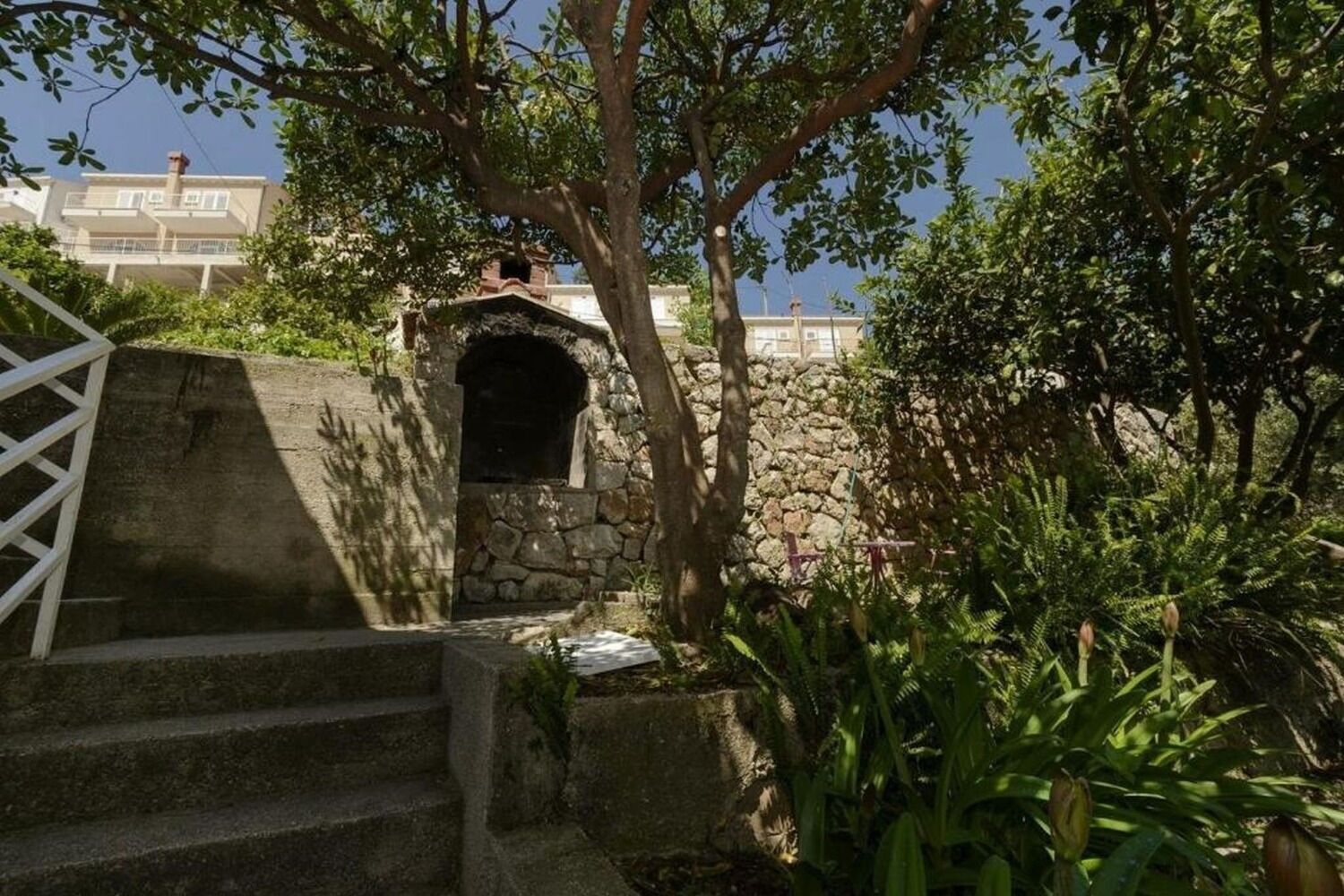 A stone staircase leading to a small arched entrance, surrounded by lush greenery and a white gate.