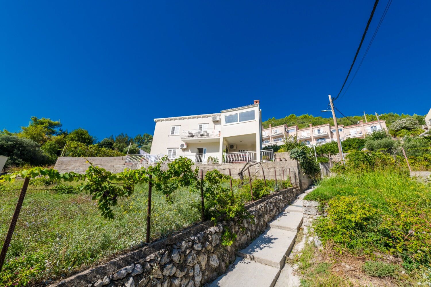 A two-story building with a balcony, a stone wall, and a pathway leading to it.