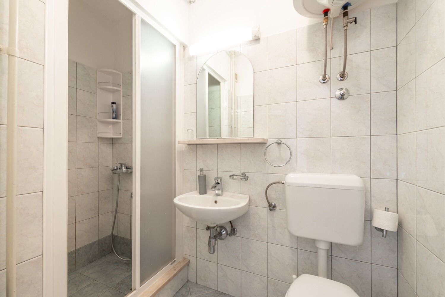 A bathroom with a shower, sink, toilet, and a mirror.