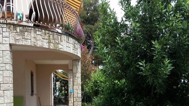 Ein Haus mit einer Steinaußenwand, einem Balkon mit Metallgeländer und einem Weg zum Eingang.
