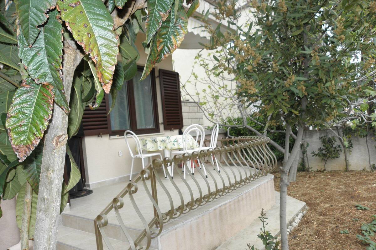A house with a covered outdoor seating area, a staircase, and a tree.