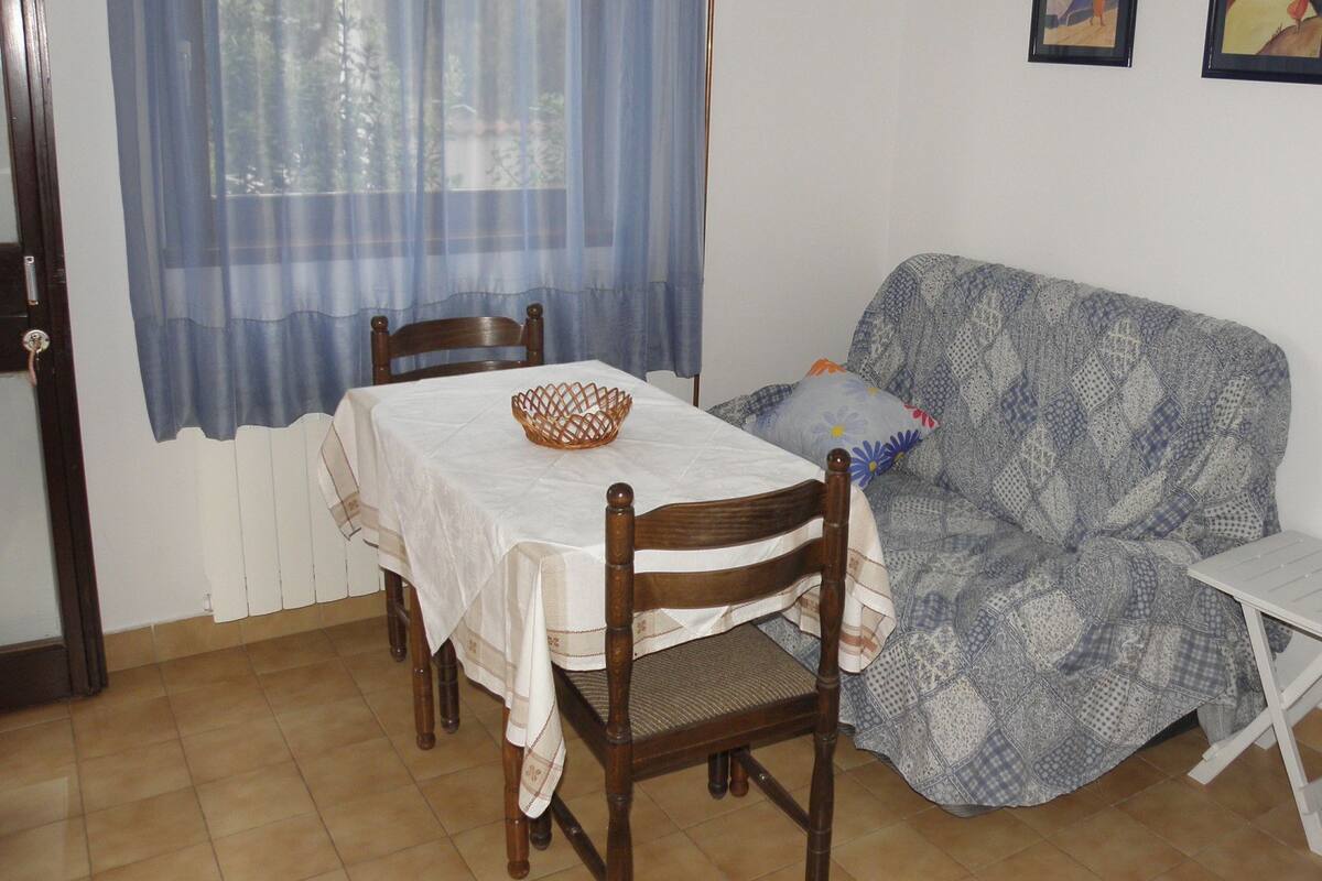 A dining area with a table set for two, a wooden chair, a patterned sofa, and a small white table.
