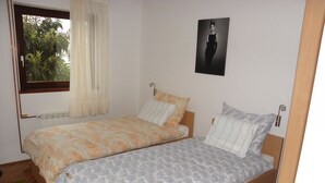 Ein Schlafzimmer mit zwei Einzelbetten, einem Vorhangfenster, einem Heizkörper und einem Poster an der Wand.