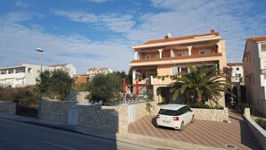 Ein mehrstöckiges Gebäude mit Sandsteinfassade, ein Auto davor und ein klarer Himmel.