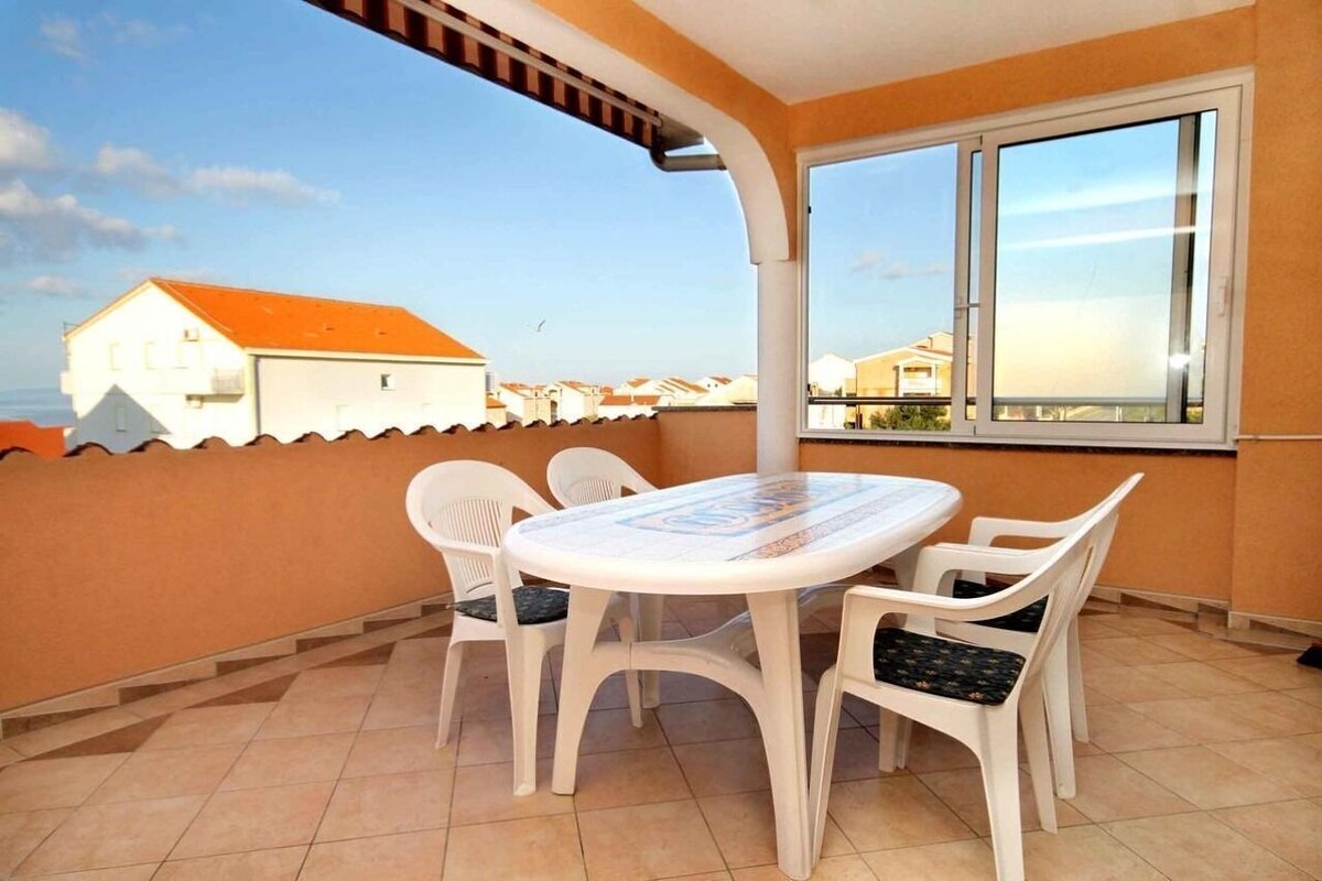 A balcony with a table and chairs, a window, and a view of buildings.