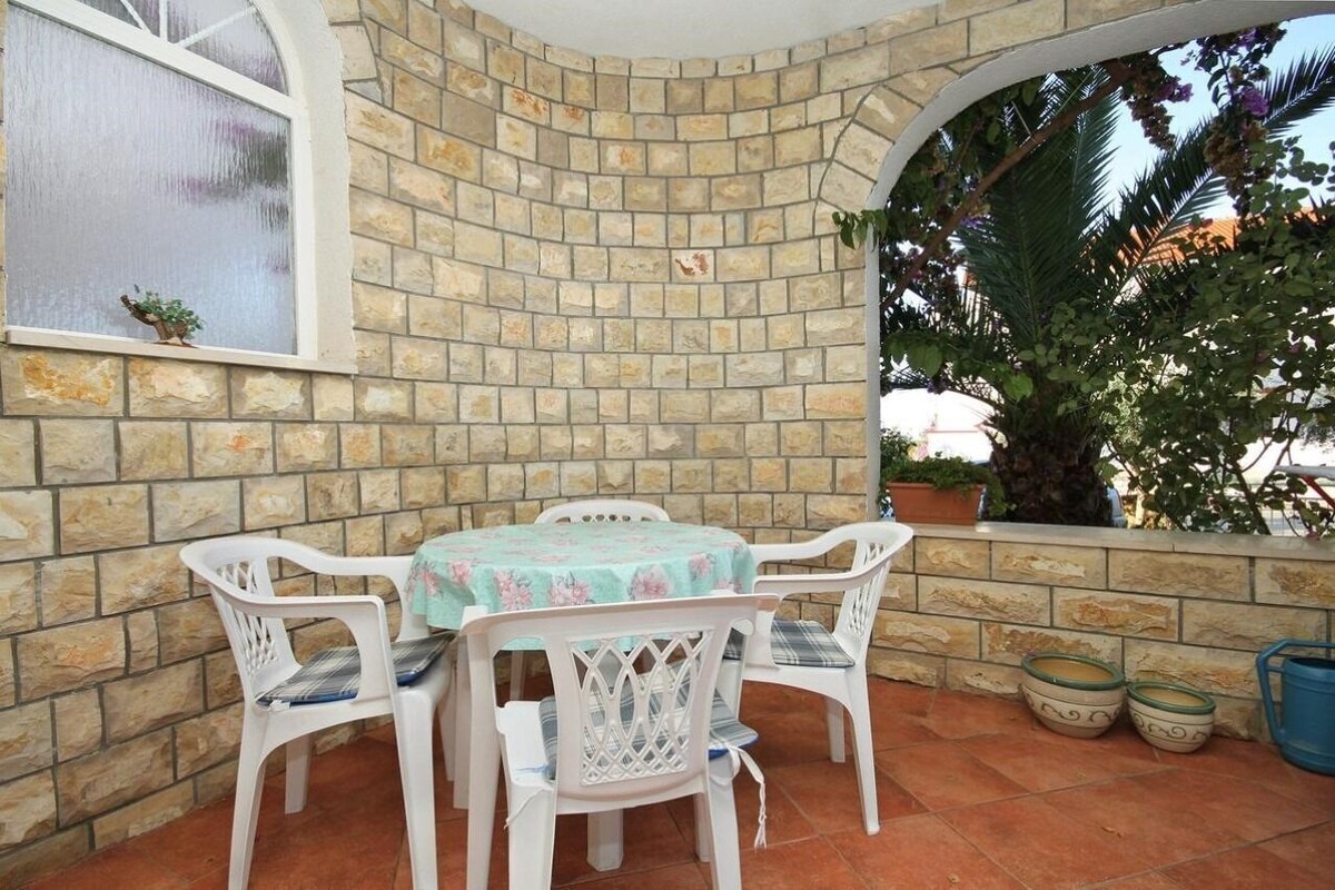 A patio with a stone wall, a table with chairs, and potted plants.