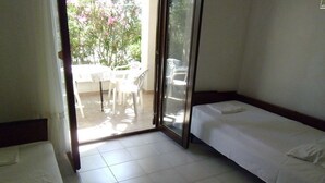 Una camera d'albergo con due letti singoli, una porta scorrevole in vetro che dà su un'area esterna con tavolo e sedie, e un pavimento piastrellato.