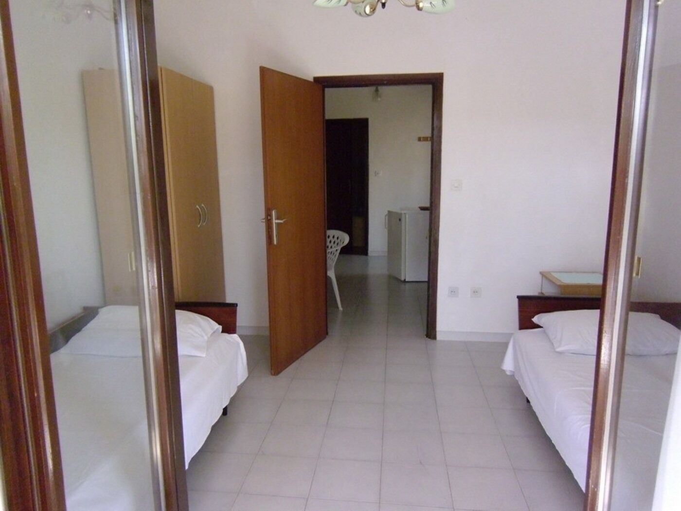 Quarto de hotel com duas camas, um guarda-roupa e uma cozinha compacta.