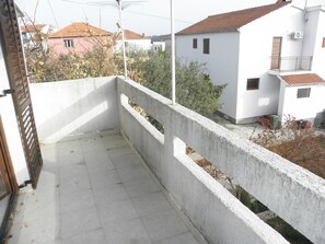 Un balcon doté d’une balustrade en béton, d’un sol carrelé et offrant une vue sur les bâtiments voisins.