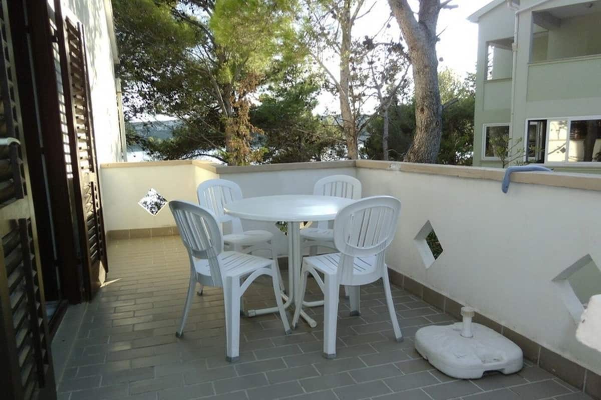Une terrasse avec une table et des chaises blanches, des toilettes blanches et un sol en briques.