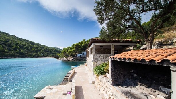 Un edificio costiero con facciata in pietra, tetto in tegole e vista sul mare.