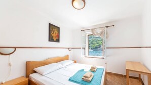 Una camera da letto con un letto di legno, un comodino, un piccolo tavolino di legno, una finestra vista mare e un quadro appeso al muro.