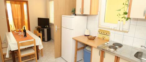 A compact kitchen with a dining area, a small refrigerator, a sink, and a window with a plant.