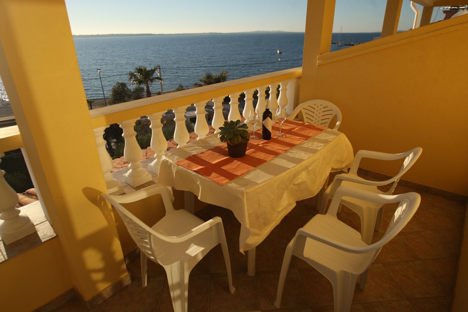 A balcony with a table set for two, overlooking a body of water.