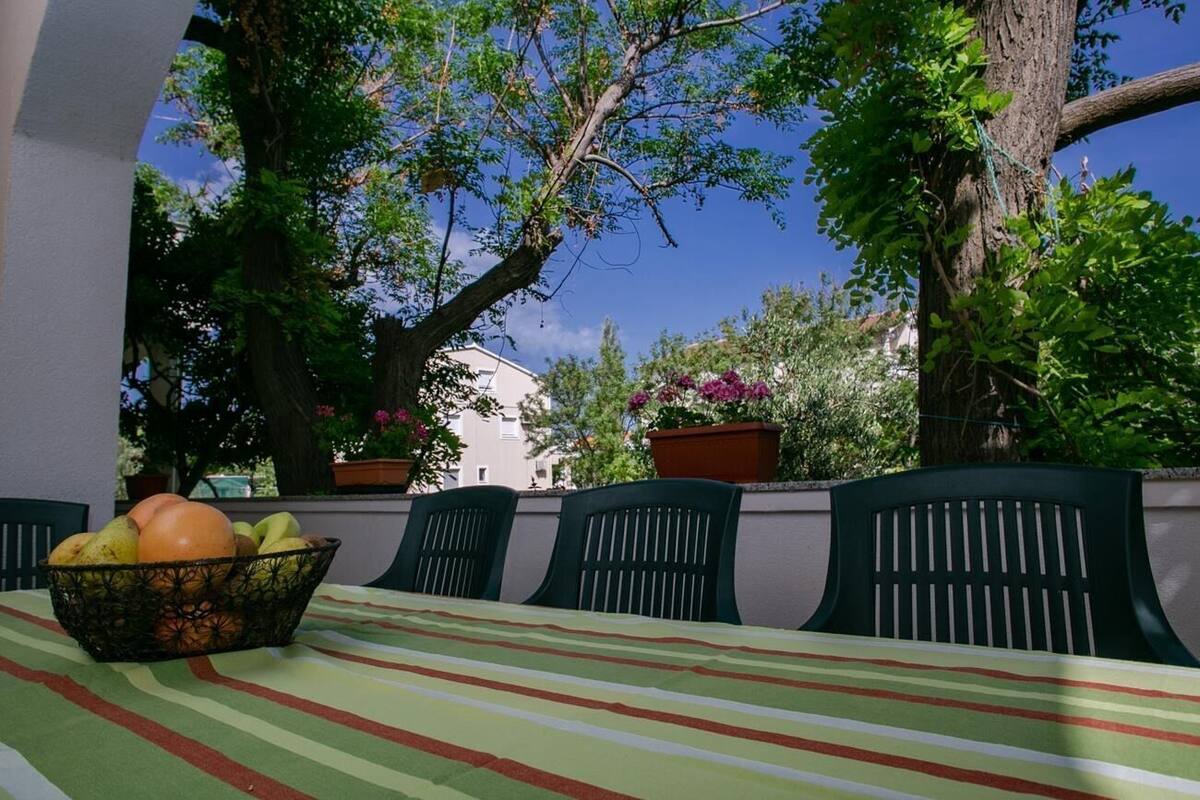 An outdoor dining area with a table and chairs, surrounded by trees and potted plants.
