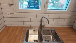 Een keuken met een dubbele roestvrijstalen spoelbak, een houten aanrechtblad en een witte betegelde spatwand.