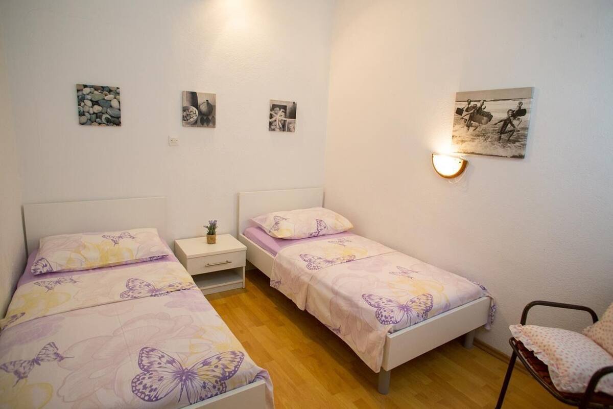 A room with two single beds, a small bedside table with a lamp, and a chair.