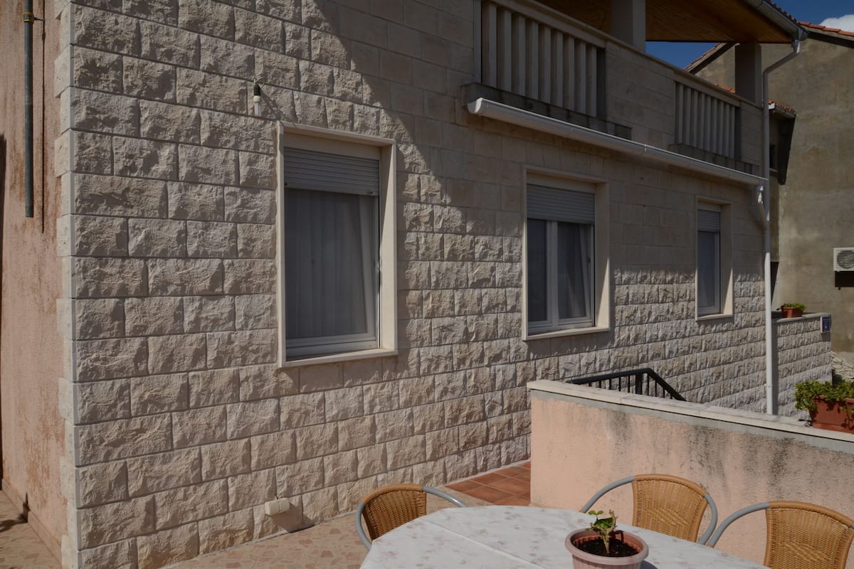 A stone building with three windows, a balcony, and a table with chairs.