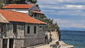 A stone building with a red-tiled roof, a stone staircase leading to a dock, and a view of the sea. - House Linker (Vis)