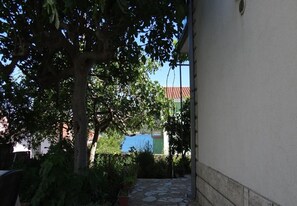 Ein schmaler Innenhof mit einem Baum, Blumentöpfen und Blick auf ein Gebäude mit blauem Dach.