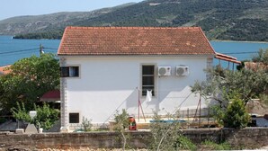 Un edificio blanco con techo de tejas rojas, dos unidades de aire acondicionado, un ventanal y una puerta.