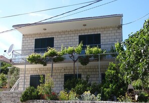 A two-story building with a balcony, surrounded by greenery and a stone wall. - Apartments Pero (Marina)