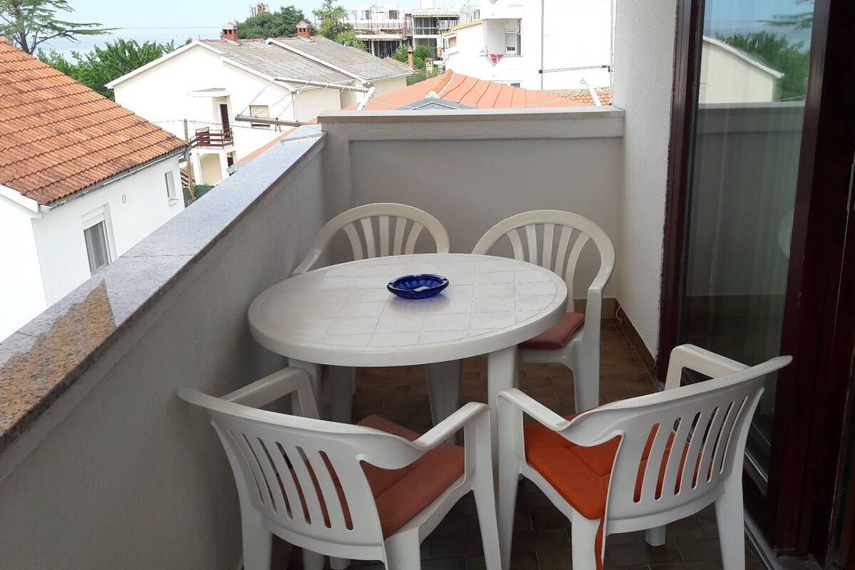 A balcony with a round table and four chairs, one with an orange cushion.