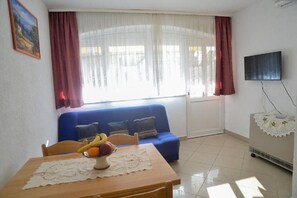 A room with a dining table, blue sofa, and a TV mounted on the wall. - Apartment Miki (Zadar)