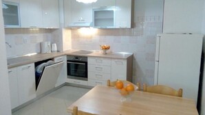 A modern kitchen with white cabinets, a built-in oven, a sink, and a dining table with oranges. - Apartment Miki (Zadar)