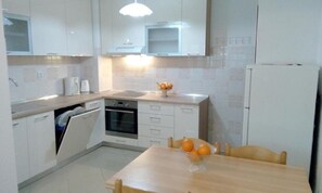 A modern kitchen with white cabinets, a built-in oven, a sink, and a dining table with oranges. - Apartment Miki (Zadar)