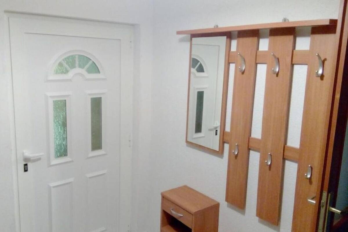 A white door with a small window, a wooden cabinet with a mirror, and a wooden shelf above the cabinet.