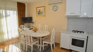 A compact kitchen with a dining area, white cabinets, a stove, and a clock on the wall. - Apartment Miki (Zadar)