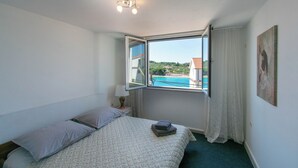 A bedroom with a bed, a window with curtains, a bedside lamp, and a painting on the wall. - Apartments Lapa (Tisno)